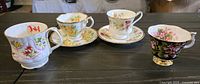 Four bone china teacups with matching saucers on table, displaying various floral patterns and styles.
