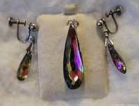 Photo showing a pair of screw back earrings and a matching pendant, all featuring long teardrop-shaped iridescent faceted crystals.