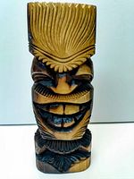 Front-facing image showing carved tiki facial features and textured hair/headdress.