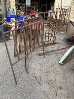 Photo of metal arbour side rails and benches outside on pavement, showing rust and wear.