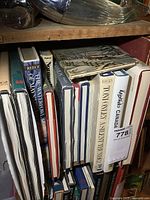 Photo of multiple large hardcover art books on a shelf showing spines with titles such as 'The Winter Book', 'Norman Rockwell','Country As I See It', and a very old scrapbook on top.