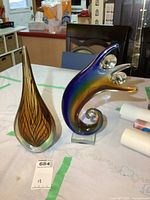 Pair of art glass figures on table showing amber teardrop with leaf pattern and colorful abstract figure with orbs