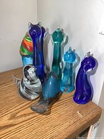 Seven colorful Murano art glass figurines on a wood surface near a white wall.