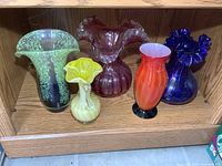 Five art glass vases on wooden shelf showing variety of colors and shapes