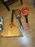All three string instruments displayed: vintage balalaika and two small toy guitars on a wood floor.