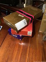 Three boxed Avon Barbie dolls stacked on a wooden table, with visible gold colored box and pink black ribbon mark.