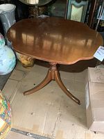 Wooden side table with scalloped rectangular top on pedestal base with caster wheels, minor wear visible.