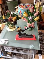 Three cast iron items on a glass table: a colorful tulip bouquet door stop, a cast iron nutcracker with a figure, and a fruit basket door stop.