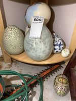Photo showing 5 collectible eggs on a wooden shelf with varied colors and materials, including porcelain, glass, and crackled finish eggs.