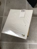 Closed white binder on floor with an auction lot sticker on the front