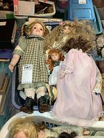 Photo of basket containing four porcelain dolls wearing various dresses and wigs, showing details of clothing and faces