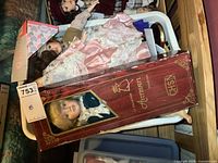 Basket of porcelain dolls showing one boxed La Collection Artisan doll and several loose dolls in vintage clothing.