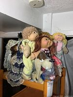 Photo showing multiple Cabbage Patch dolls and porcelain dolls on a shelf, highlighting the diversity of dolls in the lot.