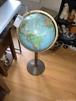 Full view of vintage globe showing Americas facing forward, wooden stand, and metal base on hardwood floor near furniture.