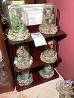 Photo showing full display shelf with six cottage collectibles, two under glass domes, certificates visible at back