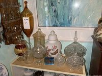 Overview of various glass items including tall amber compote, candy dishes, urn, and small teapot on shelf.