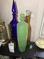 Set of three large glass decanters and an amber vase arranged on a black table against a light wall, showing color and shape variety.