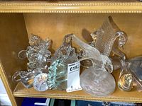 Photo showing six heavy glass figures on a wooden shelf, includes a lion, an eagle with wings spread, a swan with curved neck, and others. The eagle is the tallest figure around 8 inches.