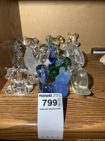 Eleven glass animal paperweights on wooden surface including bears, birds, deer, turtle, rabbit, whale, dolphin in clear, frosted white, blue and green glass.