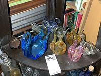 Shelf with seven glass swan dishes of various colors and sizes, arranged together on a curved wooden shelf.