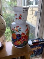 Front angle showing floral and bird designs on white glass vase with gold rim.