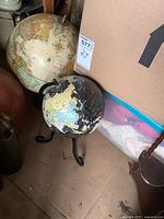 Two world globes on the floor next to boxes and furniture; one cream colored, one black colored.