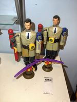 Two Inspector Gadget action figures on display showing front view with arms extended and accessories such as rocket packs and purple glider.