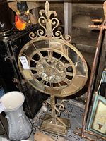 Full view of large gold-tone resin standing clock with ornate scrollwork and Roman numerals on its face, showing signs of tarnish.