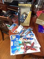 Photo showing Marvel and DC collectibles including two card books, multiple Marvel candy dispensers, and a boxed Black Adam DC Comics figurine on a table.