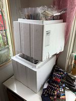 Two sturdy white polystyrene foam boxes stacked, each filled with plastic sleeves containing the matchbooks and covers.