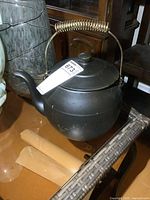 Full view of the black McCoy tea kettle with metal handle on shelf.