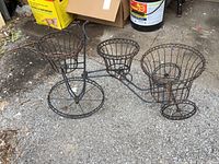 Side view of the metal tricycle plant stand showing three wire baskets for plants arranged on the frame.