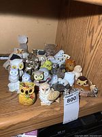 Photo of multiple owl figurines arranged on a wooden shelf showing variety in size, color, and material.