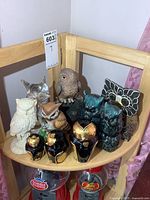 Top shelf corner wooden shelf with various owl figurines of resin, pottery, metal and glass arranged together.
