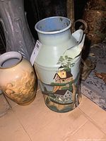 Front and side view of the cream can showing hand-painted lighthouse, houses, trees, clouds, and sky details.