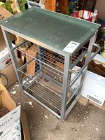 Metal serving cart angled view showing glass top, metal frame, wire baskets, and handle.