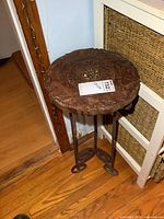 Side view of the round carved wood top side table showing metal legs and the detailed carved wooden top.
