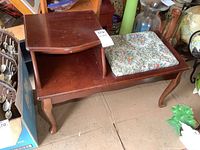 Vintage wooden telephone table with small drawer, shelf, and cushioned seat showing top and shelf area with drawer.