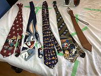 All five ties laid out horizontally: four fabric cartoon character ties and one brown wooden tie