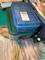 Stacked plastic totes with lids, one blue and translucent on top of a green one, placed on a fabric surface.