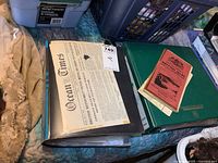 Two green binders filled with vintage papers and ephemera, with a glimpse of a newspaper clipping, plastic sleeves visible