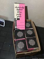 Top view of the lot showing 6 original vintage electrically lighted 12 oz party glasses in their original boxes with decorative black and pink packaging with white text.