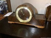 Front view showing wooden mantle clock with Roman numerals and two keyholes on dial.
