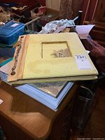 Two stacked vintage postcard albums, top album is light yellow with decorative starfish cover, sitting on wooden desk.