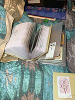 Thick postcard album lying open on a quilted bedspread, thick and filled with many postcards in plastic sleeves