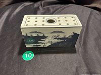 Top view of rectangular blue and white flower frog showing multiple holes and central circular hole with detailed rim pattern for flower placement.