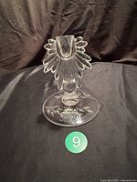 Front view of vintage clear glass candlestick with flame style petal elements and etched floral base on black fabric background.