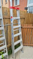 Full view of Werner 6' aluminum ladder leaning against wooden fence showing overall condition and structure.