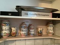 Group of five vintage Italian labeled ceramic canisters on wooden shelves.
