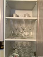 Three shelves showing various vintage glassware and ceramic cups arranged inside a cabinet.